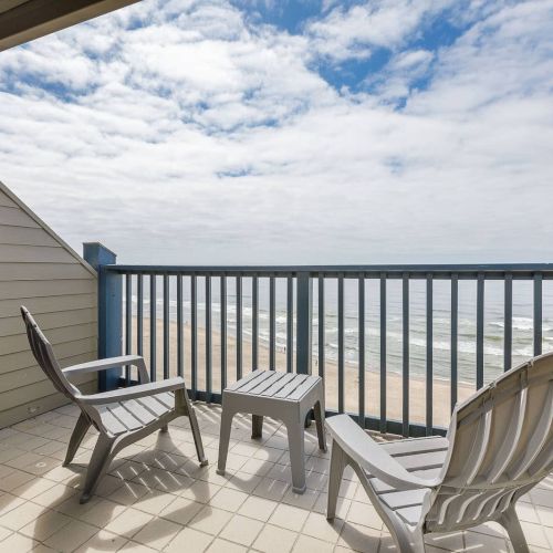 Oceanfront porch with two white chairs and a small table overlooking waves under a cloudy sky.