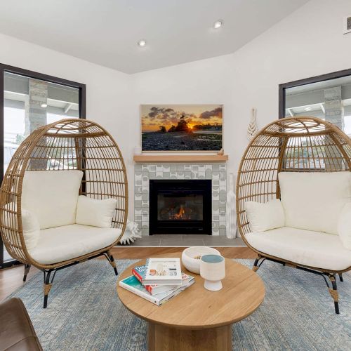 Bright lounge with two rattan egg chairs, a round coffee table, and a fireplace under a sunset wall print.