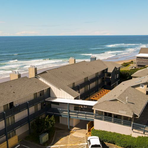 Oceanfront view with a long stretch of beach, rolling waves, and rows of seaside buildings under a blue sky.