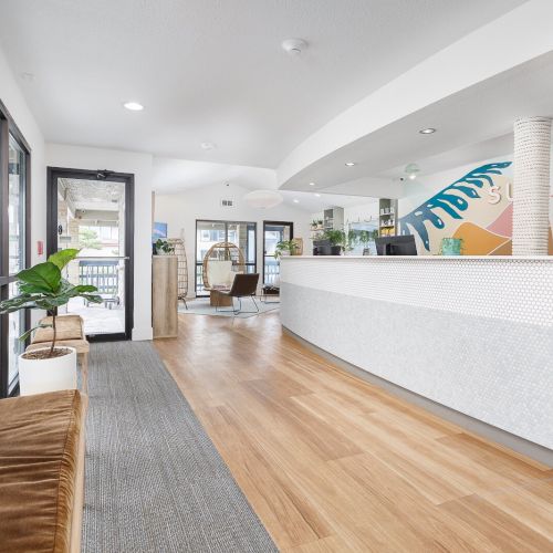 Bright modern office lobby with wood floors, plants, windows, and a reception wall mural reading &ldquo;... FLAND&rdquo;.